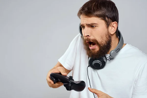 Hombre con auriculares gamepad jugando tecnología de ocio blanco camiseta fondo claro —  Fotos de Stock