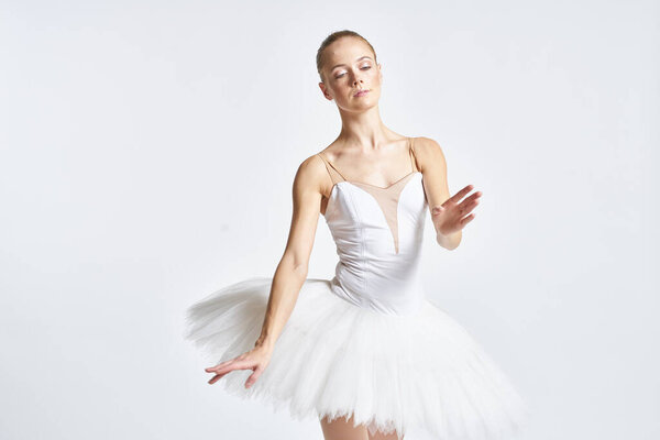 Ballerina in a white tutu performing dance exercise flexibility light background. High quality photo