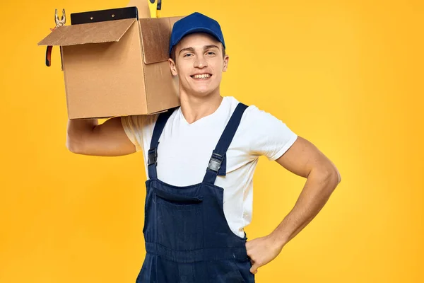 Munkás ember egyenruhában doboz kézzel szállítási rakodási szolgáltatás sárga háttér — Stock Fotó
