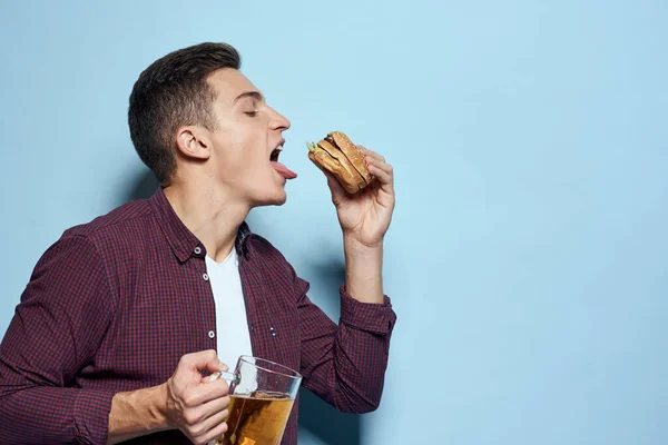 Homme ivre gai avec tasse de bière et hamburger à la main régime alimentaire mode de vie bleu fond — Photo