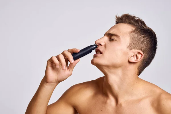 Ragazzo con un trimmer in mano rimuovere i capelli dal naso spalle nude emozioni sfondo chiaro — Foto Stock