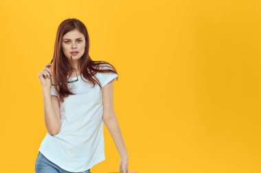 Bir kadın sandalyeye oturur ve elinde siyah bardaklarla beyaz tişörtlü kadınların moda kıyafetleri sarı arka planda kalır.