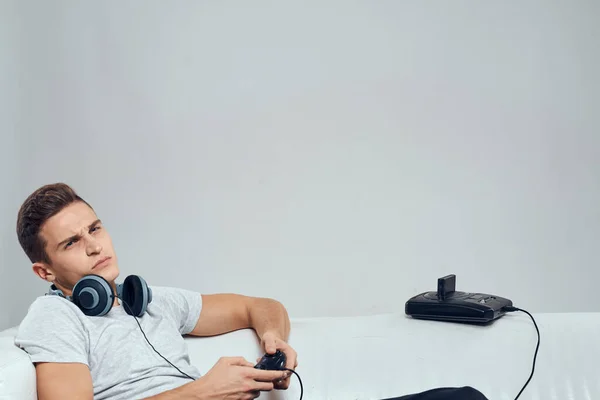 Ένας άνθρωπος βρίσκεται στο καναπέ ακουστικά gamepad κονσόλες τεχνολογία ψυχαγωγία βιντεοπαιχνίδια — Φωτογραφία Αρχείου