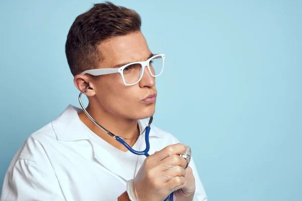 Ένας γιατρός με ρόμπα και γυαλιά κρατά ένα στηθοσκόπιο στα χέρια του σε μπλε φόντο. — Φωτογραφία Αρχείου