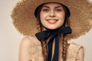 Siyah kurdeleli, saman şapkalı ve bej arka planda kırpılmış manzaralı şirin bir kız.