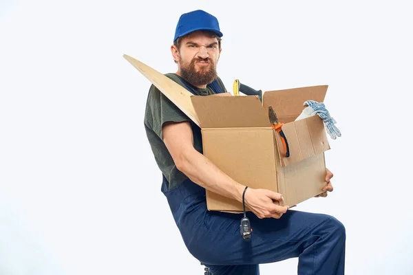 Lavoratore uomo in uniforme con una scatola nelle sue mani strumenti consegna servizio luce sfondo — Foto Stock