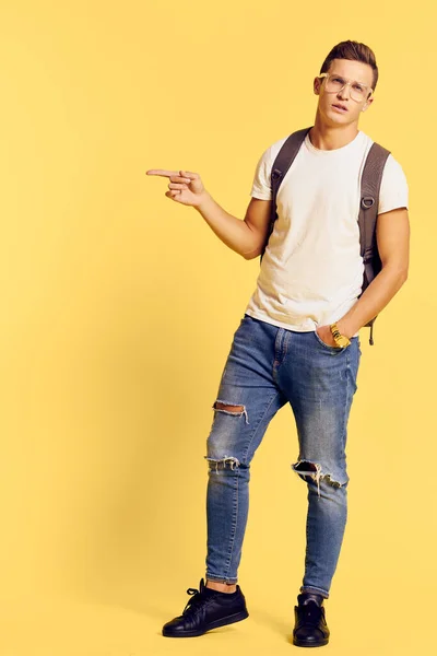 Bell'uomo in bianco t-shirt zaino sul retro jeans vestiti alla moda stile moderno gioventù giallo sfondo — Foto Stock