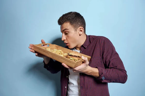Άνθρωπος με ξύλινη παλέτα fast food τηγανητές πατάτες χάμπουργκερ πείνα διατροφή τροφίμων μπλε φόντο — Φωτογραφία Αρχείου