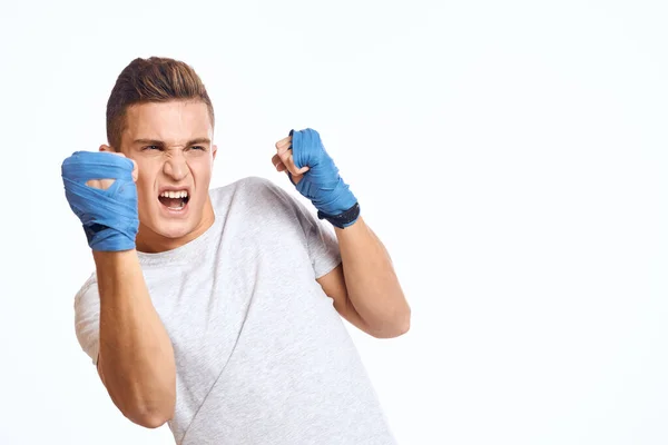 sporty male boxer in blue gloves practicing punches on a light background cropped view