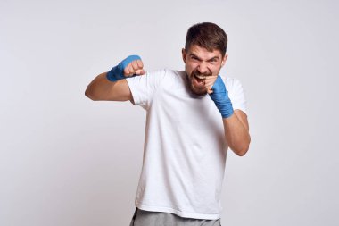 Beyaz tişörtlü sporcu. Kollarında mavi bandaj var. Egzersiz yapıyor.