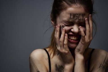 Hüsrana uğramış bir kadın vücudunda çirkin yazıtlar ve gri bir arka plan portresi üzerinde siyah bir tişört var. 