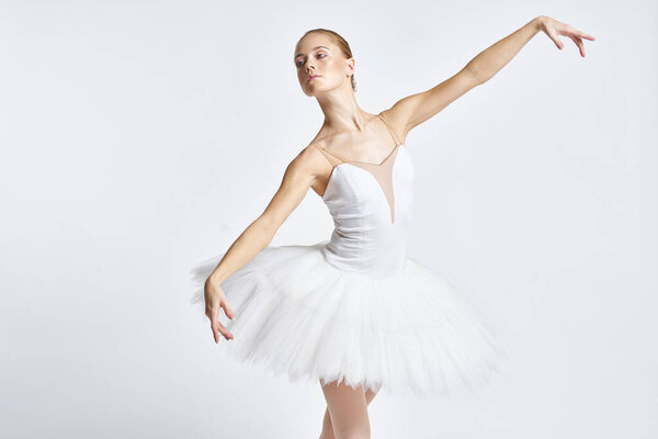 Ballerina in a white tutu performing dance exercise flexibility light background. High quality photo