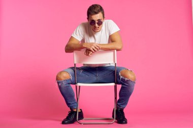 Beyaz tişörtlü ve kot pantolonlu bir adam, modern tarz pembe izole edilmiş arka planda oturuyor.