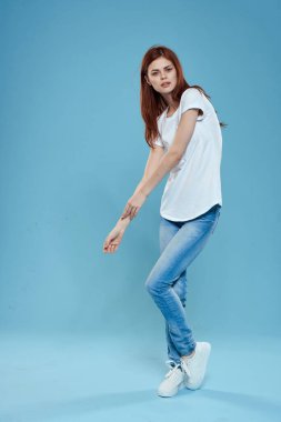 Beyaz tişörtlü, mavi kot pantolonlu, tam gelişmiş stüdyo mavi arka planlı güzel bir kadın.