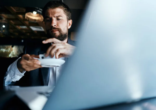Homem de negócios sentado em um café com uma xícara de café em suas mãos na frente de uma comunicação de tecnologia de laptop — Fotografia de Stock