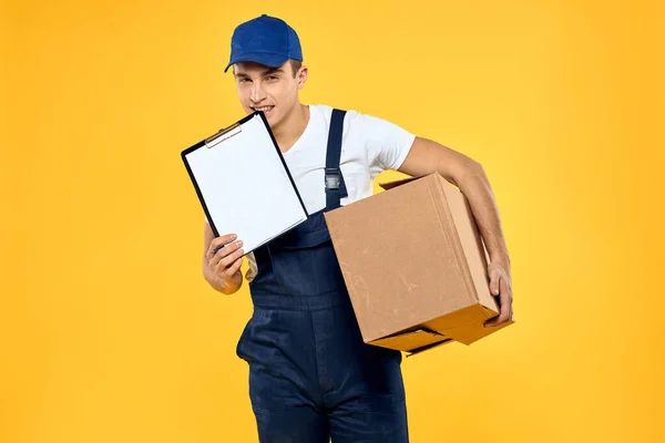 Pracujący człowiek w mundurze z pudełkiem dostawy usługi załadunku żółty tło — Zdjęcie stockowe