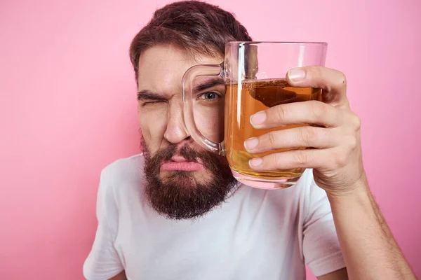 Pembe arka planda büyük bir bardak birayla sarhoş bir adam ve kalın sakallı rahat bir tişört. — Stok fotoğraf