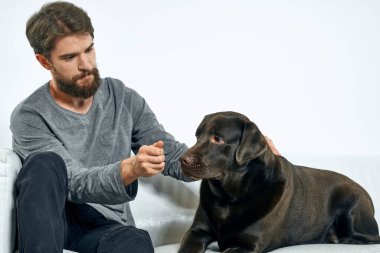 Beyaz bir kanepede siyah köpeği olan bir adam. Arka planda, yakın planda kesilen evcil hayvan insan arkadaş duyguları. Eğlenceli.