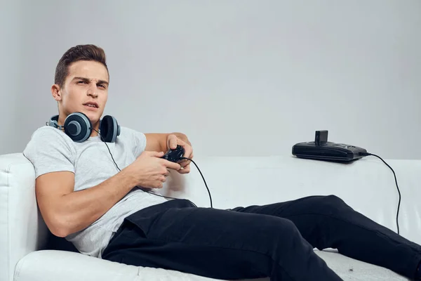 Ένας άνθρωπος βρίσκεται στο καναπέ ακουστικά gamepad κονσόλες τεχνολογία ψυχαγωγία βιντεοπαιχνίδια — Φωτογραφία Αρχείου