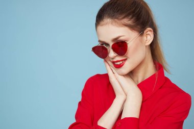 Mavi arka plandaki kırmızı gömlekli kadın yüz ve güneş gözlüklü kırmızı dudak makyajı modeli ile el ele tutuşuyor.