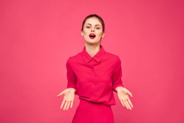 Pembe arka planda, parlak elbiseli, kızıl saçlı bir kadının portresi elleriyle el kol hareketi yapıyor.