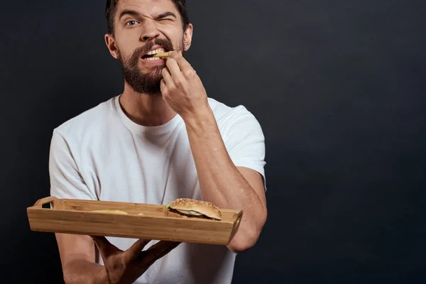 Kobieta mężczyzna z palety fast food frytki i hamburger dieta jedzenie restauracja biały t-shirt ciemne tło — Zdjęcie stockowe