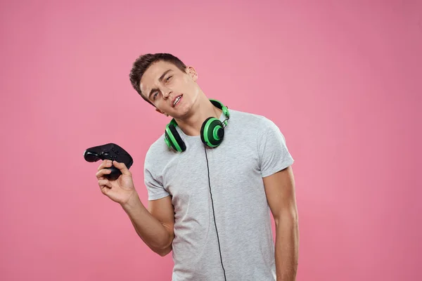 Een man met een joystick in zijn handen koptelefoon spelen spelletjes entertainment levensstijl wit t-shirt roze achtergrond — Stockfoto