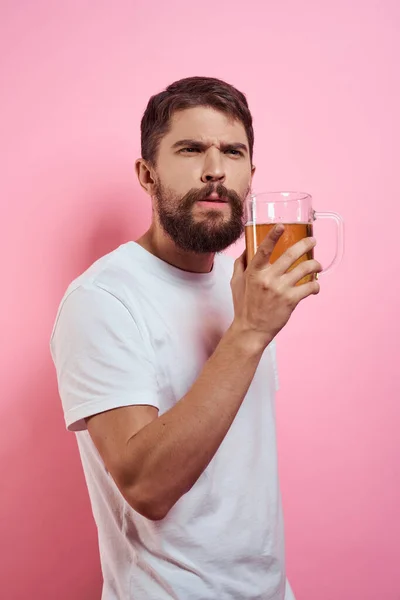 Hombre barbudo con una taza de cerveza En un fondo rosa emociones divertidas recortado vista de una camiseta blanca borracho — Foto de Stock