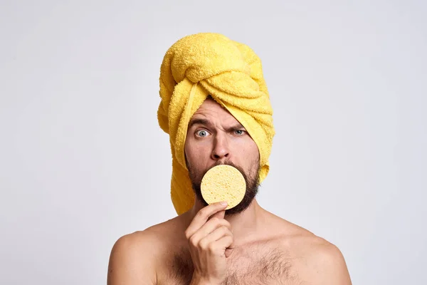 Homem com uma toalha amarela em sua cabeça ombros nus esponja pele limpa cuidados faciais luz fundo — Fotografia de Stock