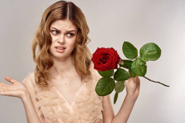 Elinde kırmızı bir gül olan çekici bir kadın açık arkaplanda yakın plan kesilmiş bir portrede.