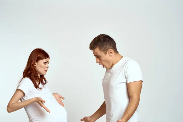 A pregnant woman and a young man are waiting for a baby on a light background emotions family love — Stock Photo, Image