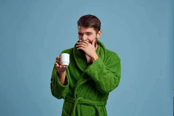 Bevroren man in een warme badjas met een kopje warme drank op een blauwe achtergrond bijgesneden uitzicht — Stockfoto