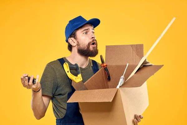 作業中の男性は黄色い背景のツールを搭載した箱を形成します — ストック写真