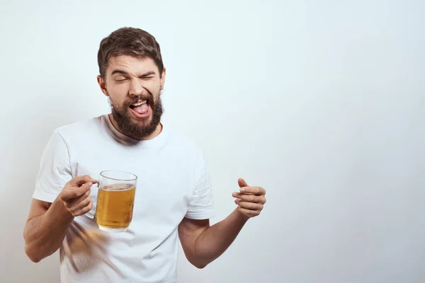 Homme avec une tasse de bière dans ses mains et un t-shirt blanc fond clair moustache barbe émotions modèle — Photo