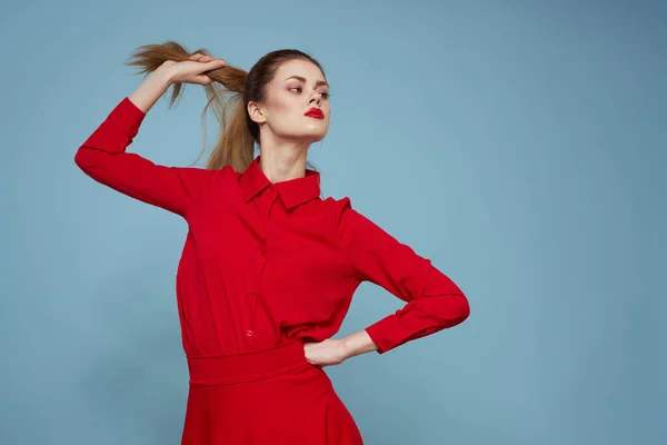 Chica feliz en ropa brillante sobre un fondo azul toca el pelo en su cabeza con las manos — Foto de Stock