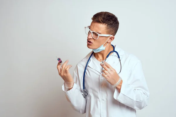 Steteskoplu gözlüklü bir doktor elinde hafif bir arka plan görüntüsü olan bir şırınga tutuyor. — Stok fotoğraf