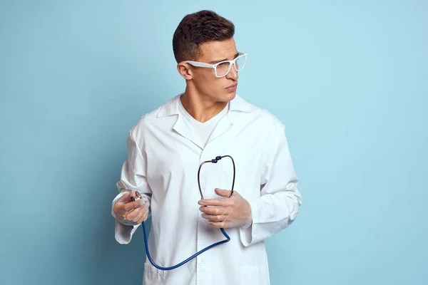 A medical worker in a dressing gown and glasses holds a stethoscope in his hands on a blue background cropped view — Stock Photo, Image