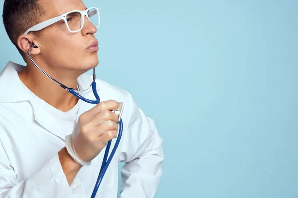 Un travailleur médical en robe de chambre et lunettes tient un stéthoscope dans ses mains sur un fond bleu recadré vue — Photo