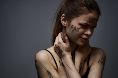 Hüsrana uğramış bir kadın vücudunda çirkin yazıtlar ve gri bir arka plan portresi üzerinde siyah bir tişört var. 