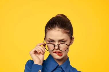 Mavi gömlekli, gözlüklü, yüzünde parlak makyajlı bir kadın elleriyle işaret ediyor.