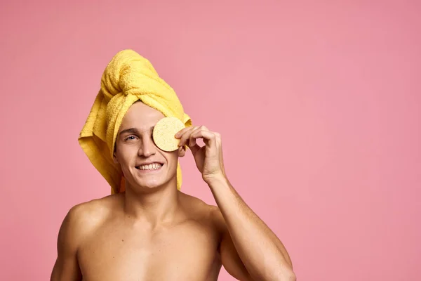Uomo con un asciugamano sulla testa e una spugna gialla nella sua procedura cosmetica mano pelle pulita del viso — Foto Stock