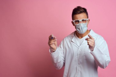 Tıbbi maskeli ve eldivenli bir doktor şırıngayı bir şırınga laboratuvarında tutuyor.