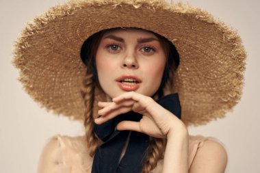 Hasır şapkalı, siyah kurdeleli ve arka planda açık bir elbise giyen hoş bir kız. Romantik bir model.