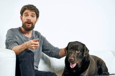 Beyaz bir kanepede siyah köpeği olan bir adam. Arka planda, yakın planda kesilen evcil hayvan insan arkadaş duyguları. Eğlenceli.