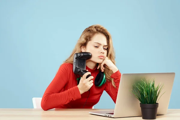 Mulher sentada em uma mesa na frente de um controlador de fones de ouvido laptop jogando estilo de vida on-line fundo azul — Fotografia de Stock