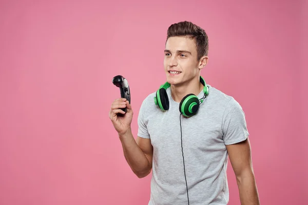 Un hombre con un joystick en sus manos auriculares jugando juegos de entretenimiento estilo de vida camiseta blanca fondo rosa — Foto de Stock