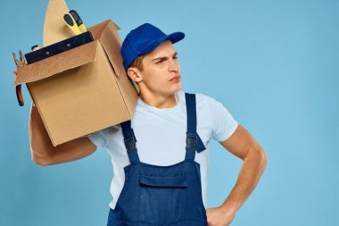 Üniforma kutusunda çalışan adam. Aletleri yükleyen kişi mavi arka plan.