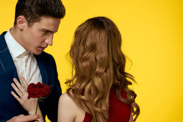 Un uomo romantico abbraccia una donna in abito rosso con una rosa in mano su uno sfondo giallo — Foto Stock