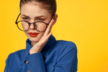 Mavi gömlekli, gözlüklü, yüzünde parlak makyajlı bir kadın elleriyle işaret ediyor.