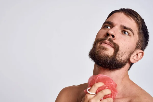 Een man met blote schouders een washandje in zijn handen schone huid nemen van een douche lichte achtergrond — Stockfoto